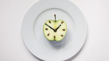 Half an apple on plate with clock hands, studio shot.